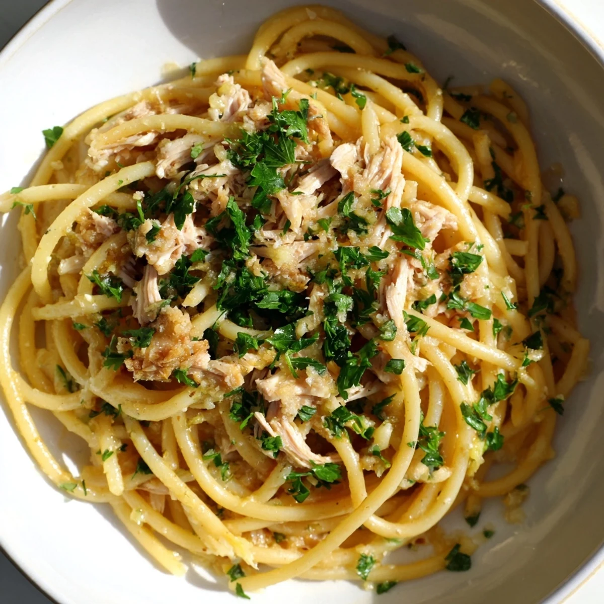 Steaming plate of Simple Garlic Butter Bucatini, topped with shredded chicken and fresh parsley.