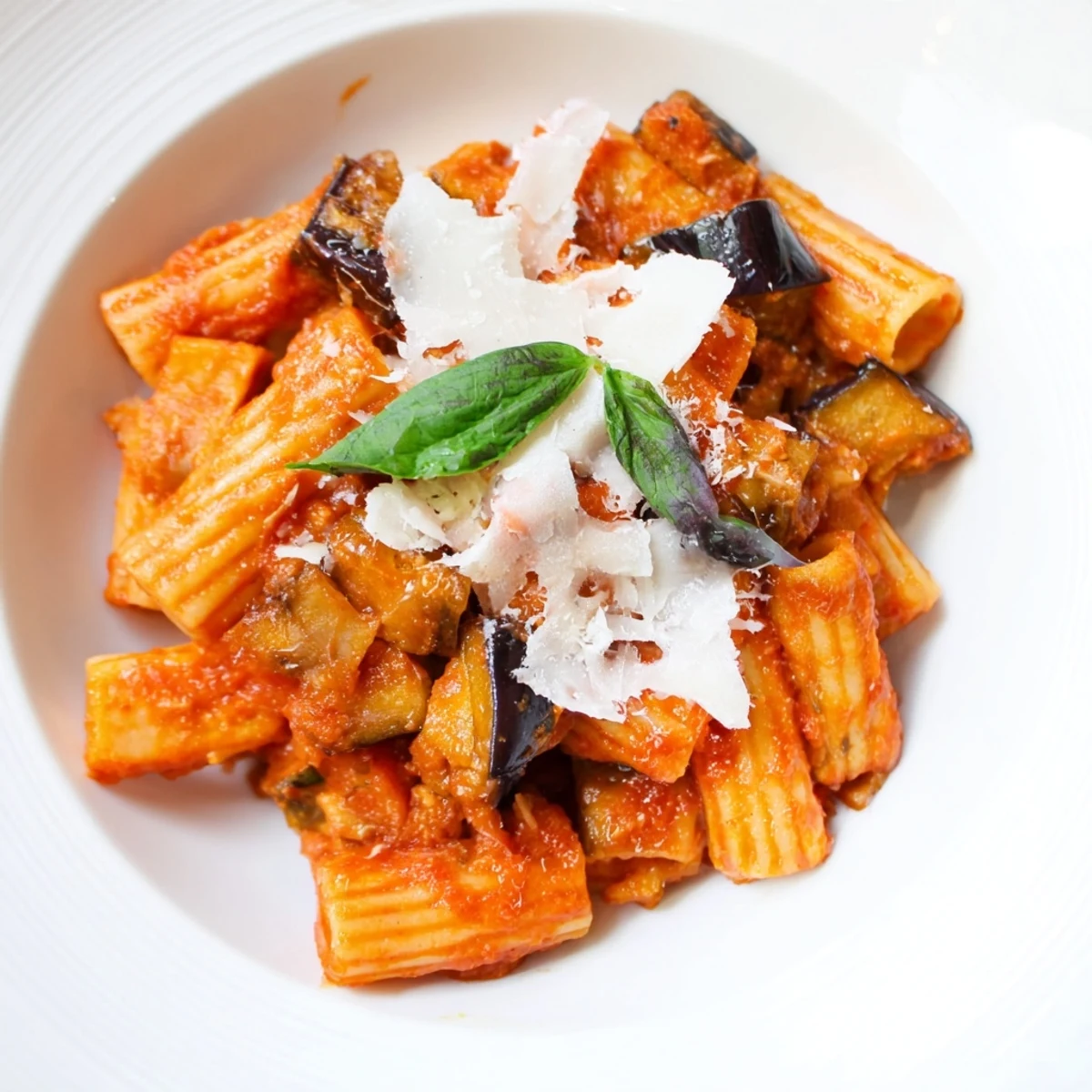 Steaming bowl of Pasta Alla Norma with tender eggplant, vibrant tomato sauce, and grated ricotta salata cheese.