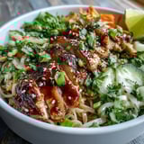 A close-up of a serving of Asian Chicken Noodle Bowl drizzled with savory sauce and lime.