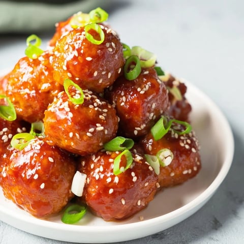 Tender, juicy Spicy Honey-Glazed Chicken Meatballs glistening in a sweet and spicy honey sauce on a plate.