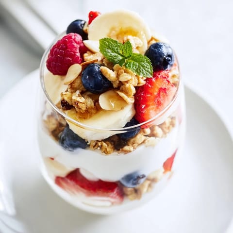Cool, layered yogurt and granola parfait glasses topped with fresh fruit and a drizzle of honey.