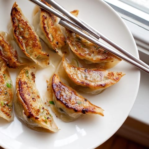 A close-up of smashed gyozas with a golden, crispy bottom and juicy pork and cabbage filling, ready to be dipped in chili oil and soy sauce.  
